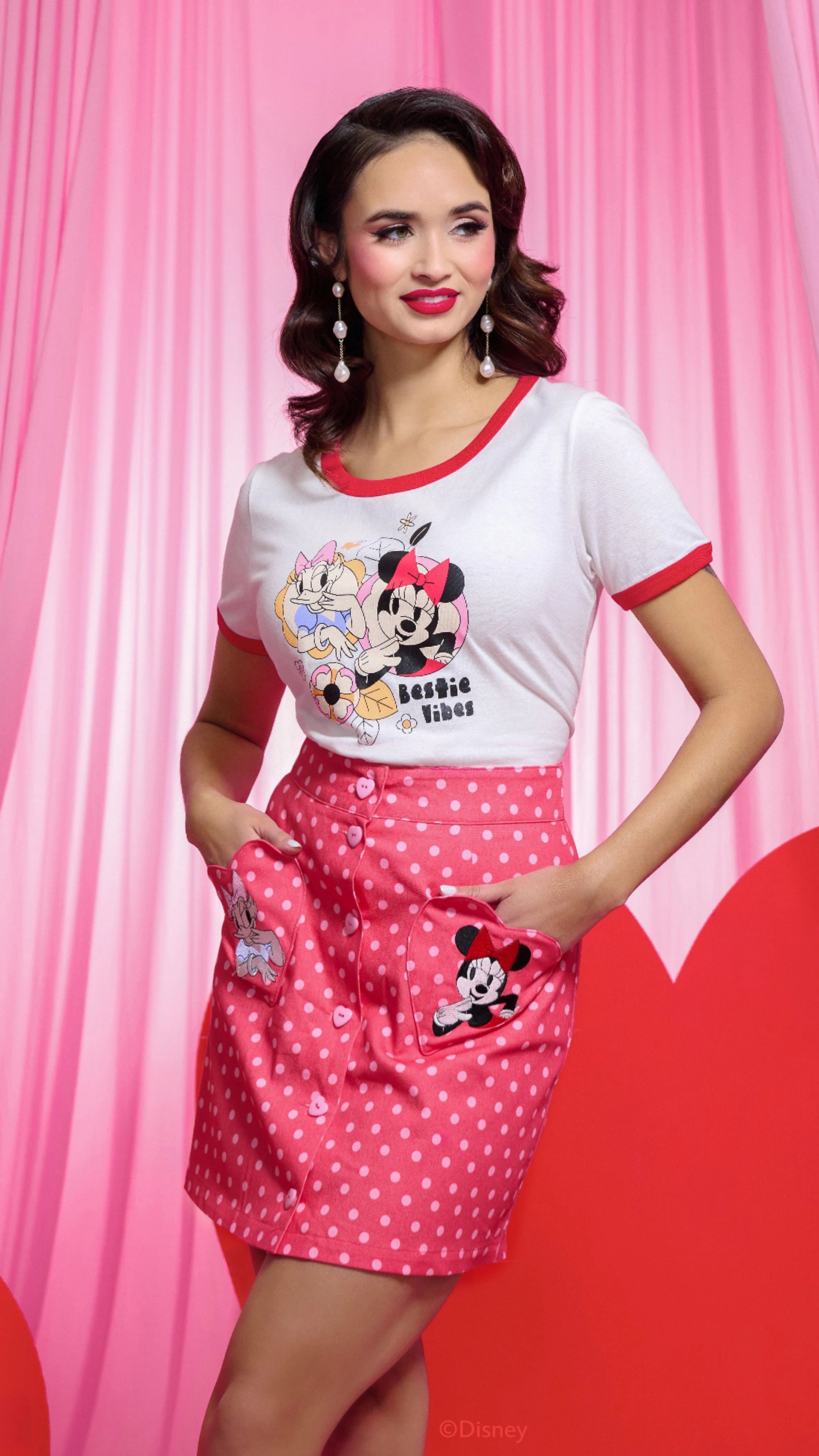Woman wearing a Minnie Mouse-themed outfit with a white t-shirt and pink skirt against a pink background.