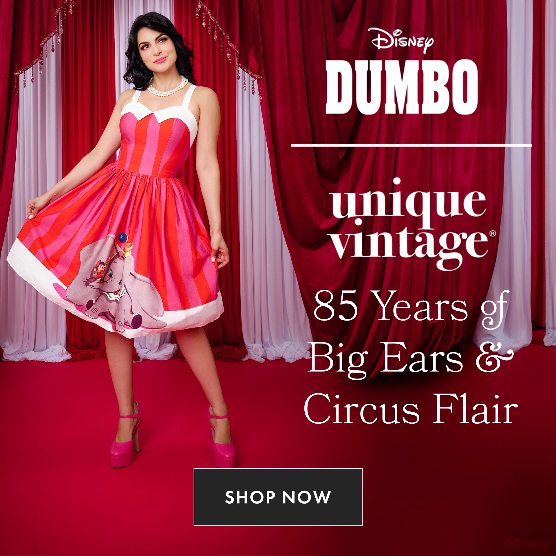 Woman wearing a red and white dress with Dumbo design in front of red curtains, Disney Dumbo branding visible.