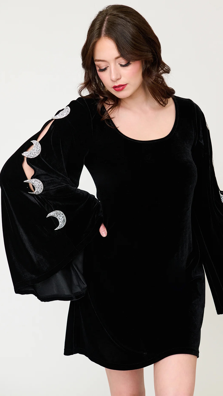 A woman wearing a black velvet long-sleeve dress with silver moon embellishments on the sleeves, photographed against a plain light background.