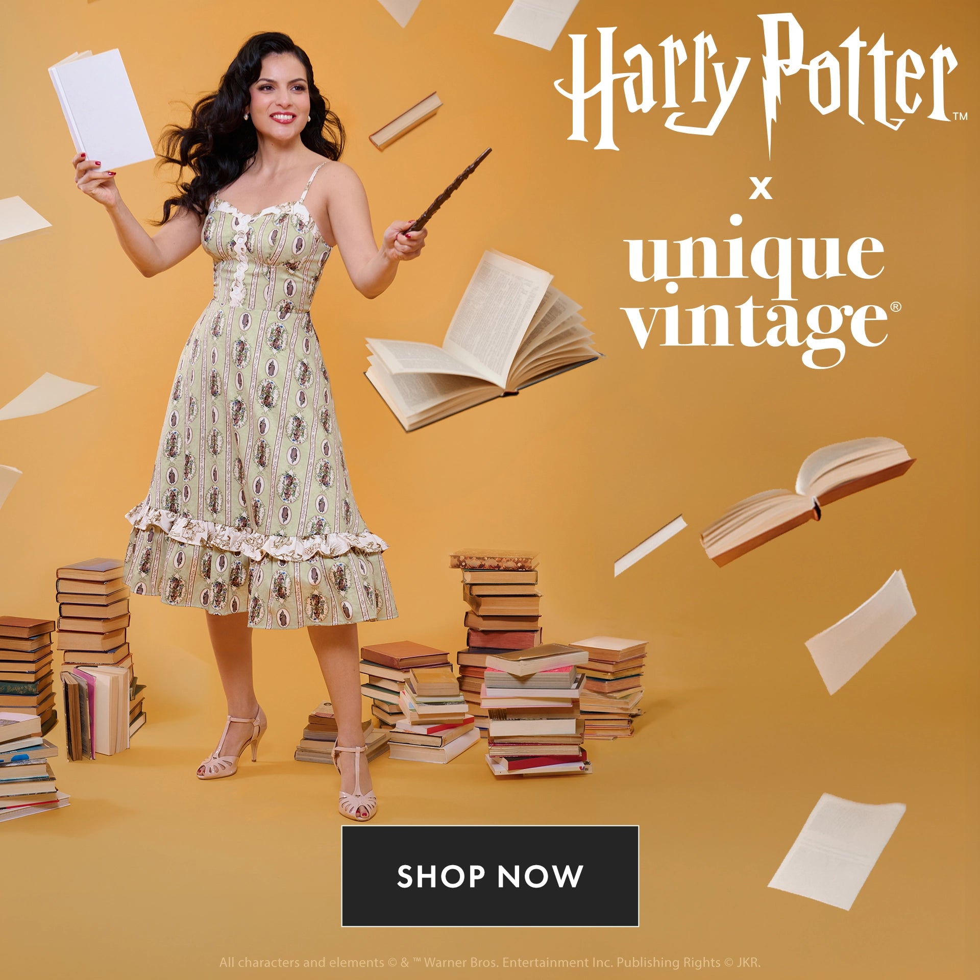 A woman in a sleeveless vintage-style dress stands in a studio setting with a warm yellow background, surrounded by floating book pages and stacks of books. She holds a wand and a sheet of paper.