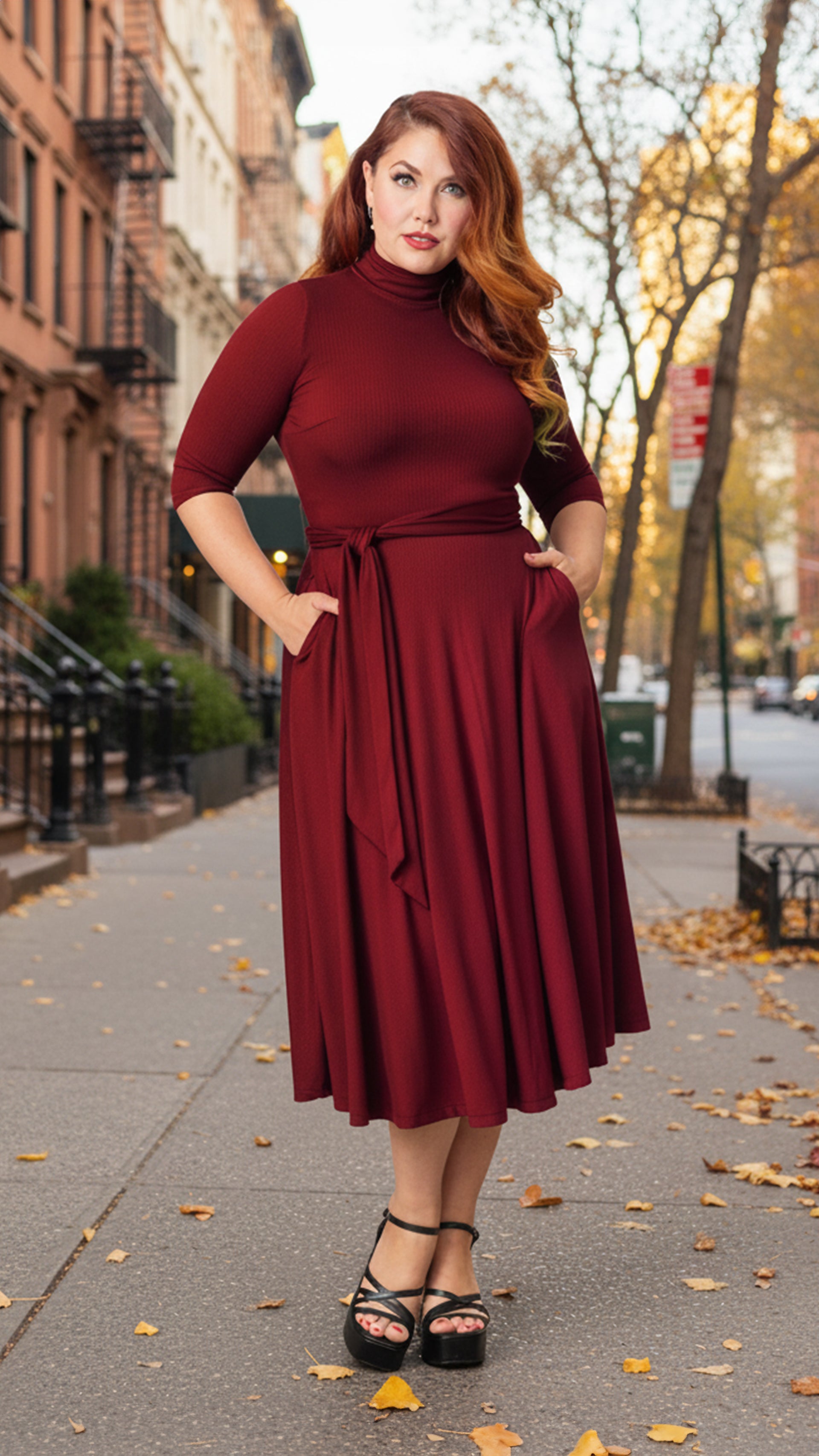 Woman wearing a burgundy dress on a city street with autumn leaves. Shop Plus Size Women's Clothing